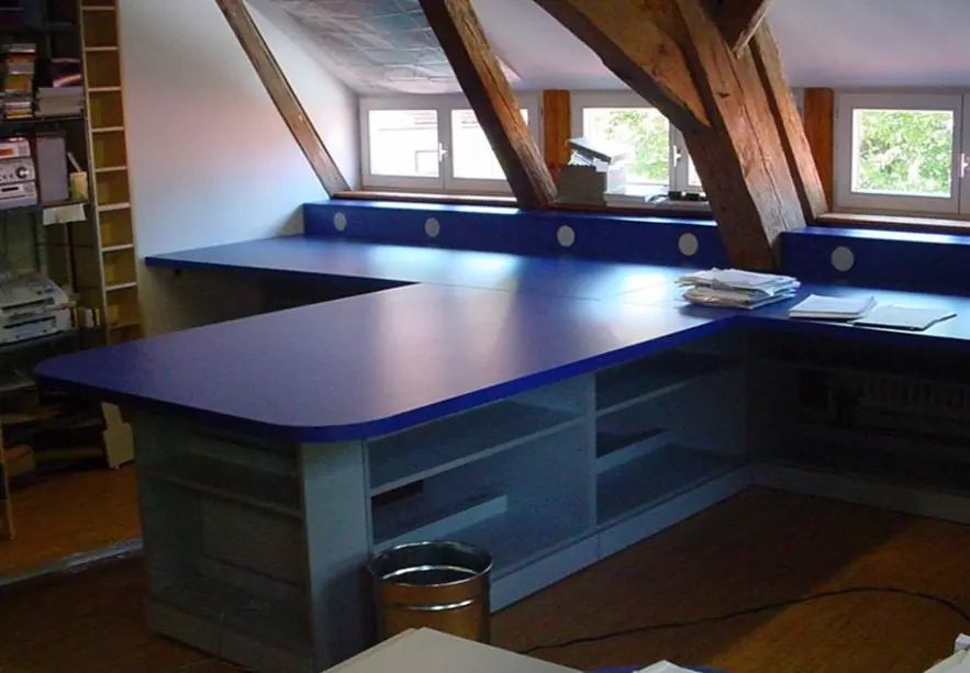 Eckarbeitsplatte mit blauer Platte und offenen Regalfächern unter einer Dachschräge mit Holzbalken