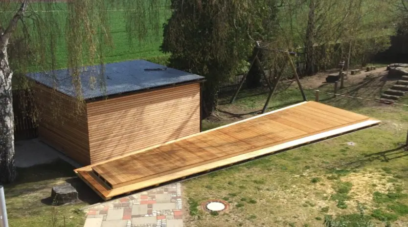 Holzdeck auf einer Wiese vor einem Gartenhaus mit Holzverkleidung